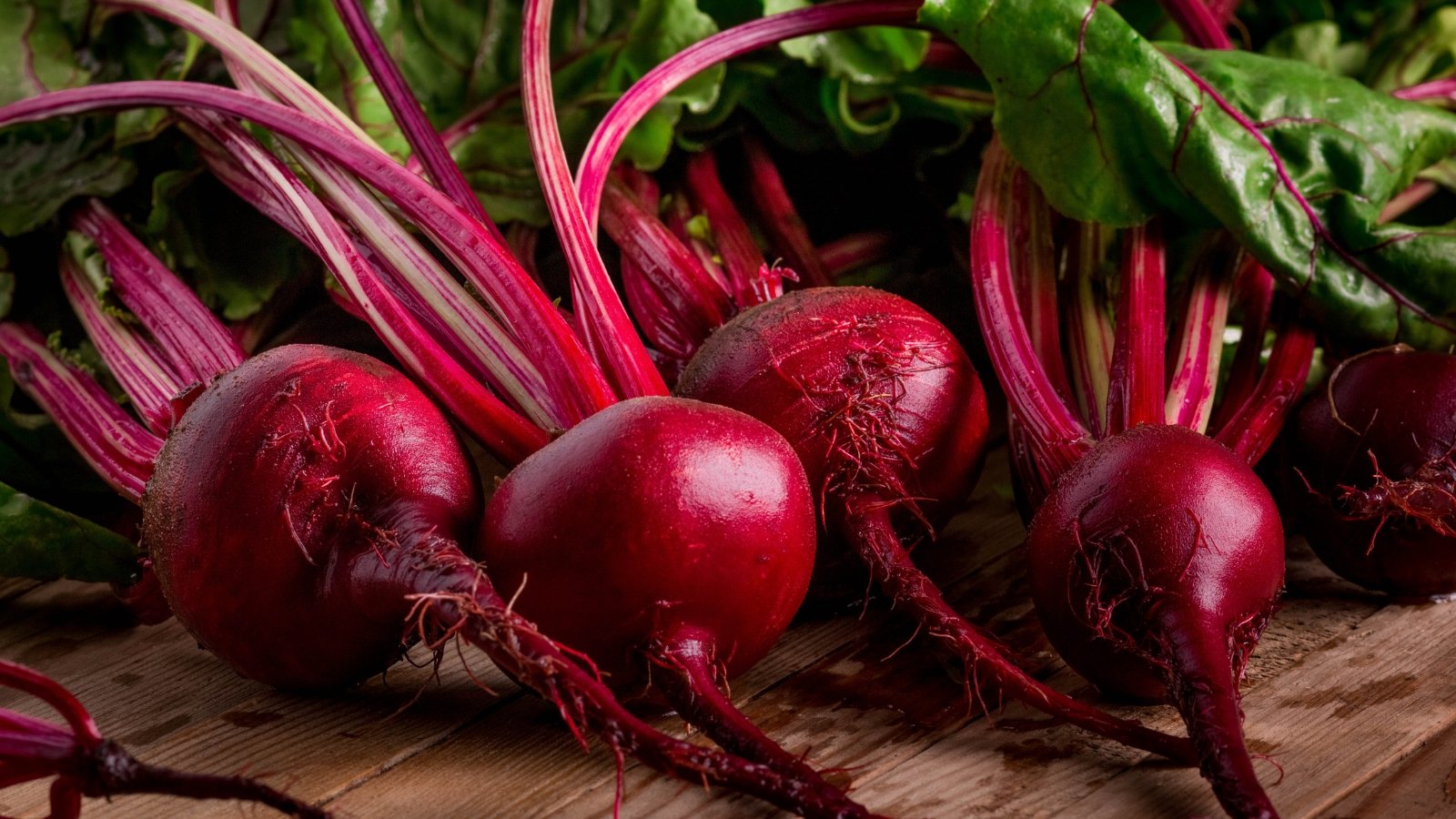 A collection of freshly picked tubers, with deep red skins and vibrant magenta stems, placed on a rustic wooden surface, with some soil clinging to the roots.